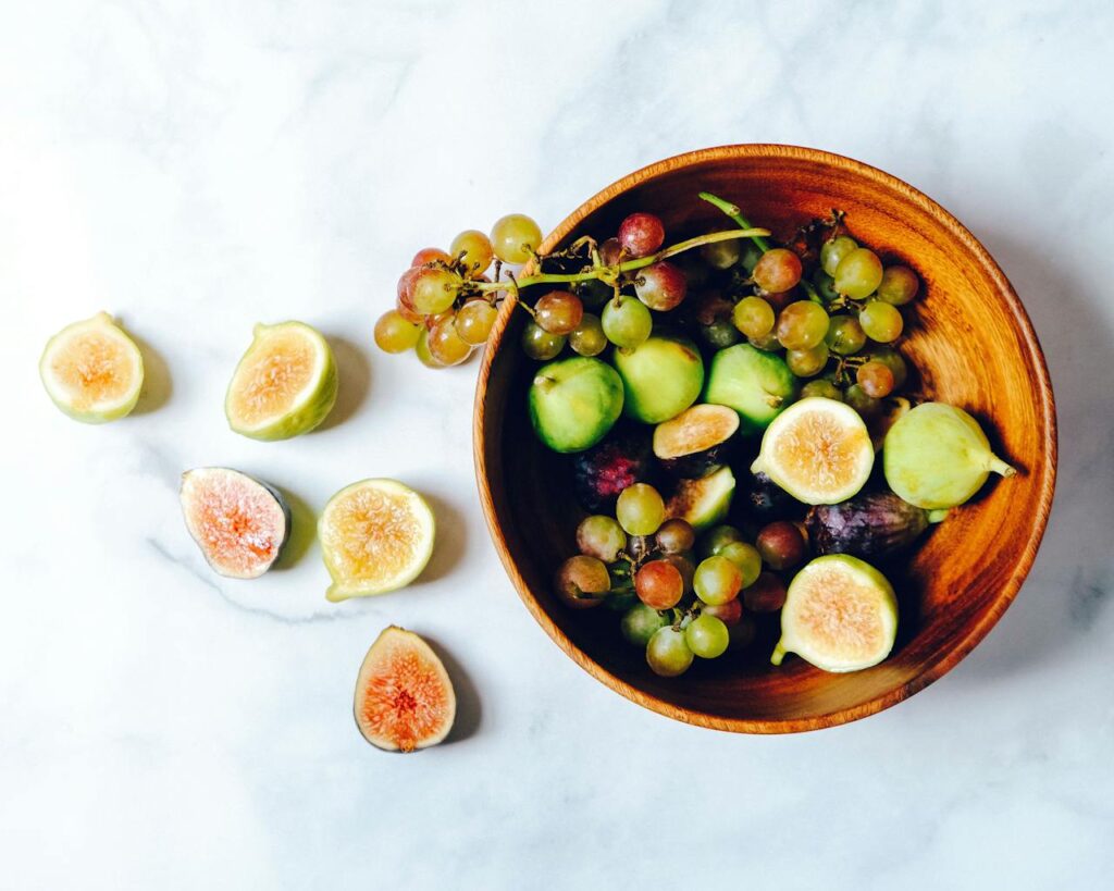 A vibrant and fresh bowl of green grapes and figs on a marble surface, perfect for healthy eating.